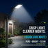 A modern outdoor LED street light mounted on a pole, casting a bright beam of light at night toward a house entrance. The scene is set in a real outdoor environment with a walkway, plants, and buildings under a dark night sky.